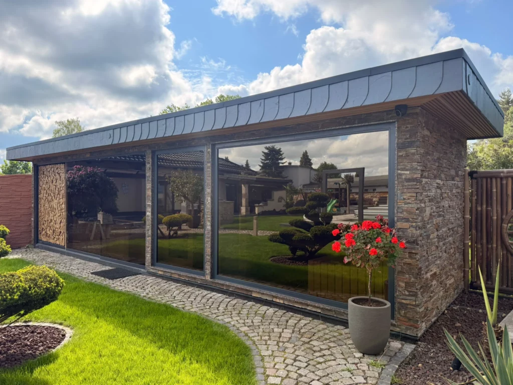 Freistehendes Saunahaus mit durchgehender Glasfront und Natursteinwand im Garten